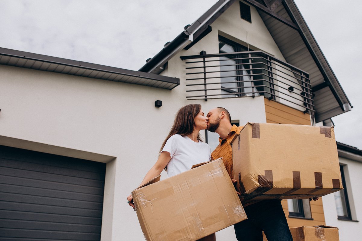 Pareja cargando cajas frente a su nueva casa